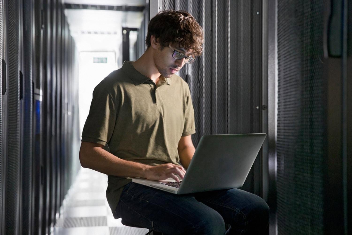 System administrator managing cloud and VPS hosting from a laptop in a server room